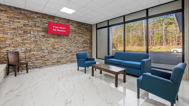 A modern waiting area with stone walls, a large window offering a view of trees and a road, and a sign indicating free Wi-Fi availability. - HomeTowne Studios by Red Roof Athens, TN (Athens)