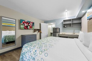 Habitación de hotel con una cama grande, un escritorio, un armario, un espejo y un televisor en la pared.