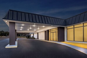 A modern building with a covered entrance, large windows, and a well-lit interior. - HomeTowne Studios by Red Roof Athens, TN (Athens)