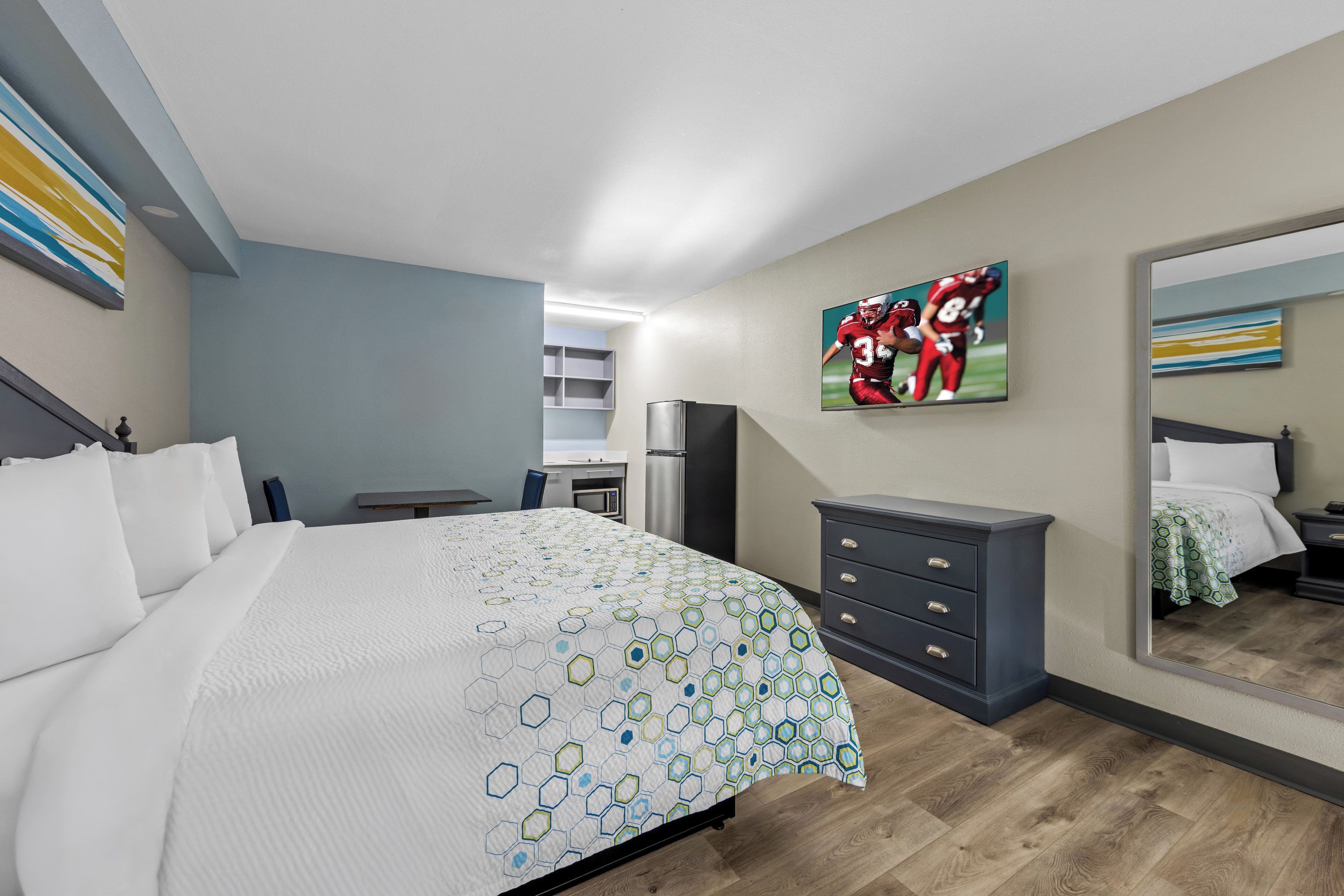 A modern bedroom with a large bed, a dresser, a TV, and a mirror.