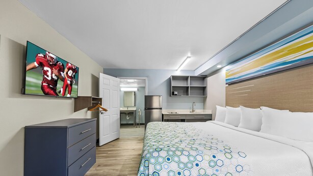 Ein modernes Hotelzimmer mit einem großen Bett, einem Schreibtisch, einem Kleiderschrank und einem Fernseher, der ein Sportspiel zeigt.
