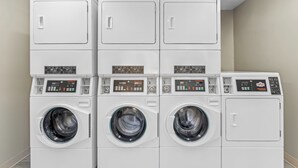 A row of stacked, white, front-loading washing machines in a laundry room. - HomeTowne Studios by Red Roof Athens, TN (Athens)