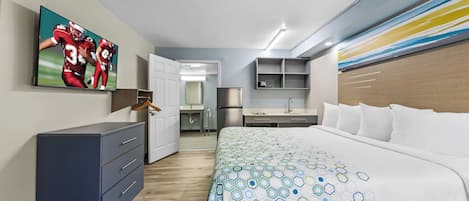 Une chambre d’hôtel moderne équipée d’un grand lit, d’un bureau, d’une armoire et d’un téléviseur diffusant un événement sportif.