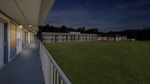 A building with a covered walkway and a grassy lawn. - HomeTowne Studios by Red Roof Athens, TN (Athens)