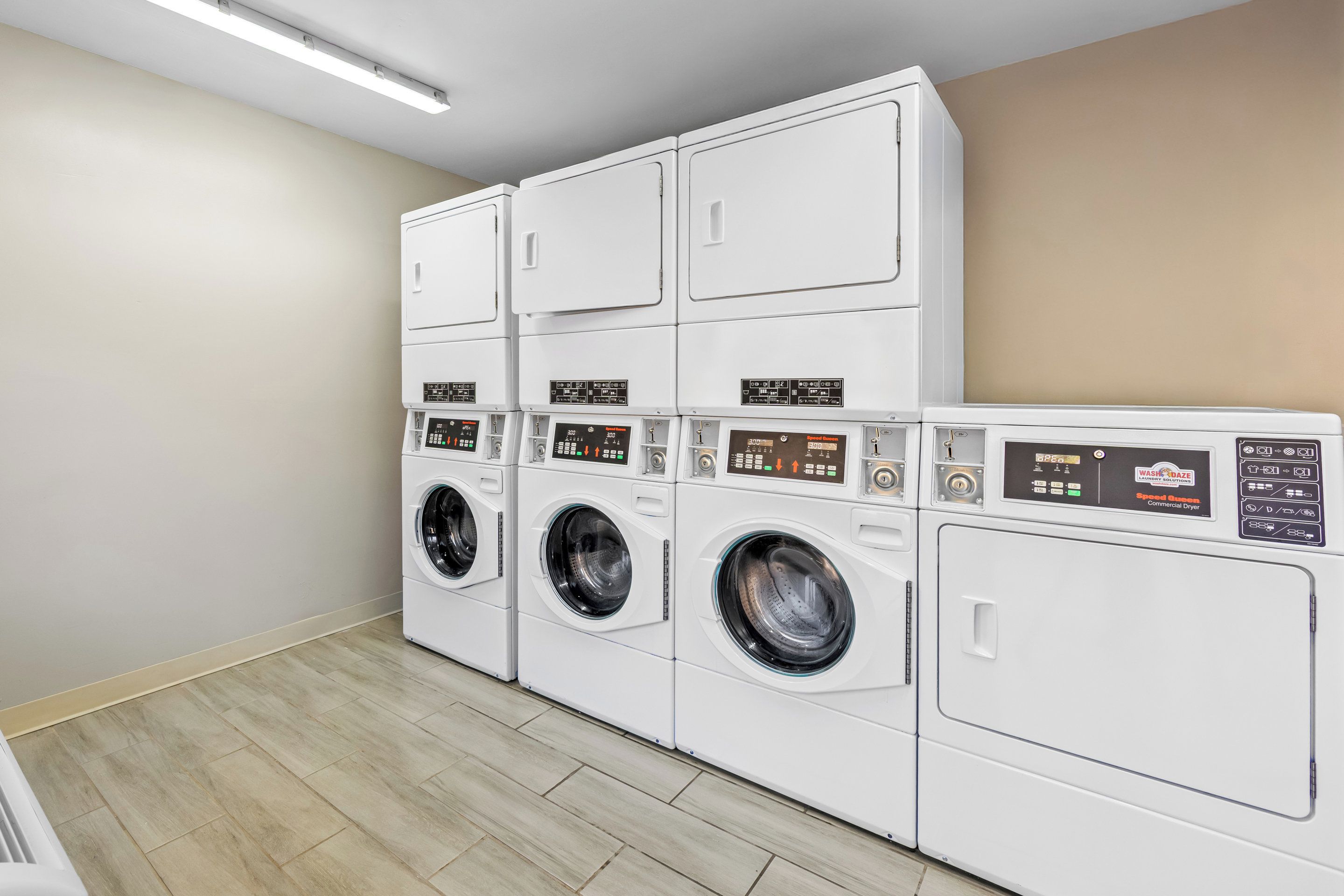 A row of white front-loading washing machines in a laundry room with beige walls and light wooden flooring.
