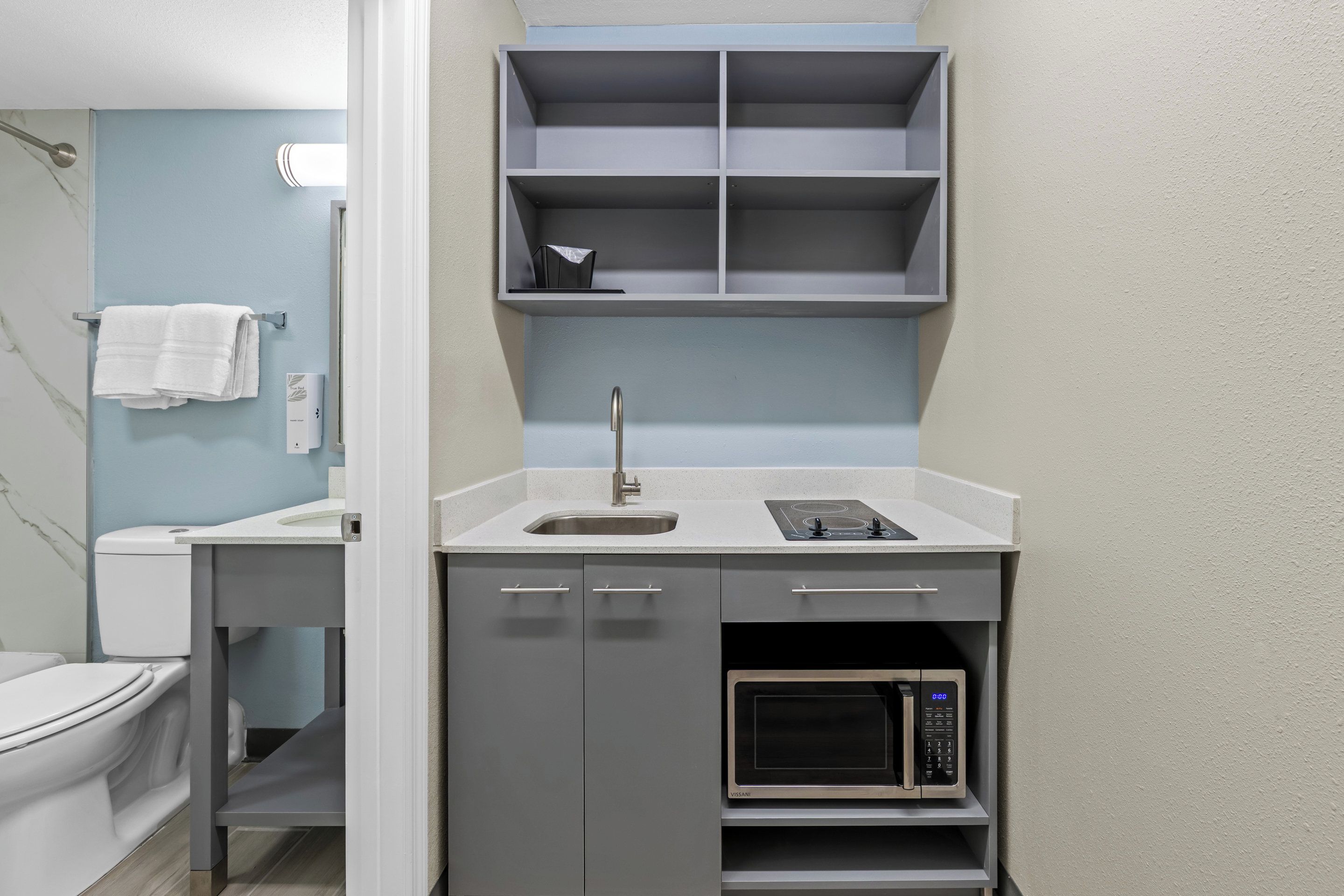 A compact kitchenette with a sink, microwave, and storage shelves.