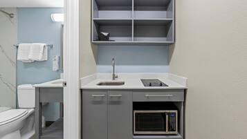 A compact kitchenette with a sink, microwave, and storage shelves.
