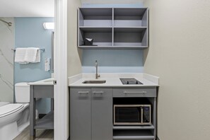 A compact kitchenette with a sink, microwave, and storage shelves. - HomeTowne Studios by Red Roof Athens, TN (Athens)