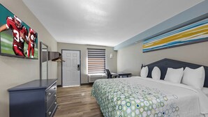 A bedroom with a bed, a dresser, a TV, and a painting on the wall. - HomeTowne Studios by Red Roof Athens, TN (Athens)