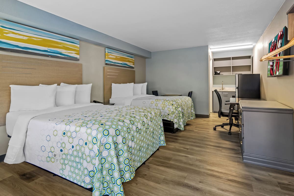 A hotel room with two beds, a desk, a chair, and a television.