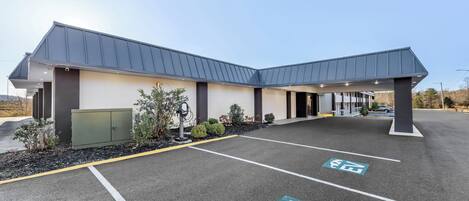 A modern building with a flat roof and a covered entrance. There are designated parking spaces for bicycles and cars.