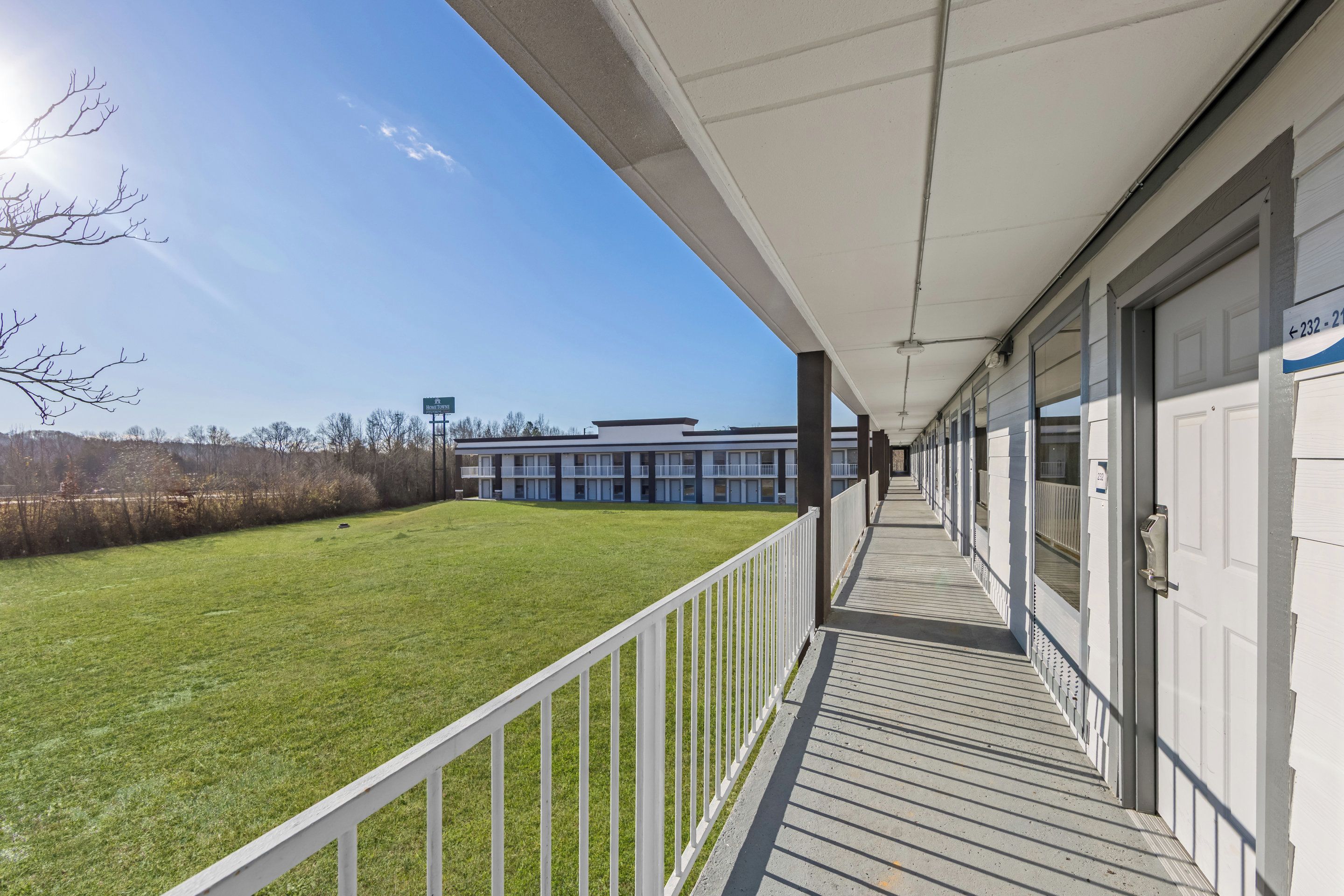 A covered outdoor area with a white railing, a grassy lawn, and a building in the background.