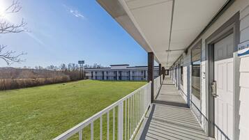 A covered outdoor area with a white railing, a grassy lawn, and a building in the background.