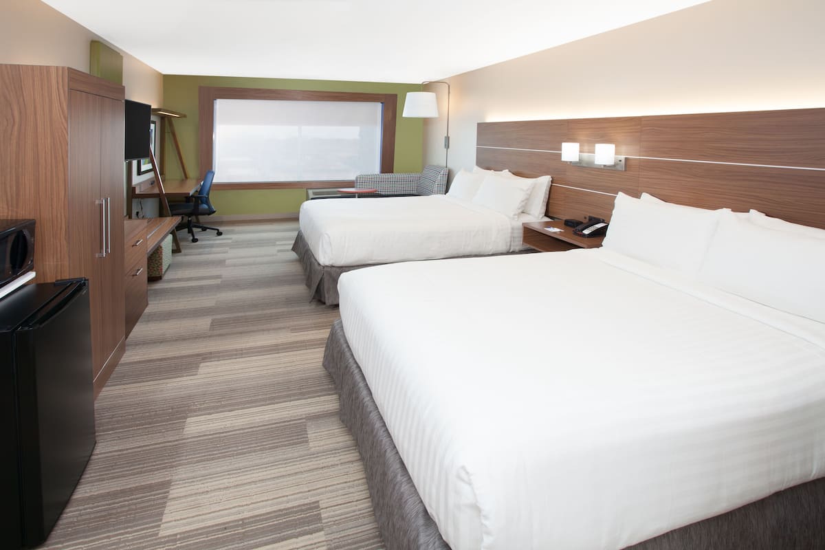 A hotel room with two beds, a desk, a chair, a TV, and a window.