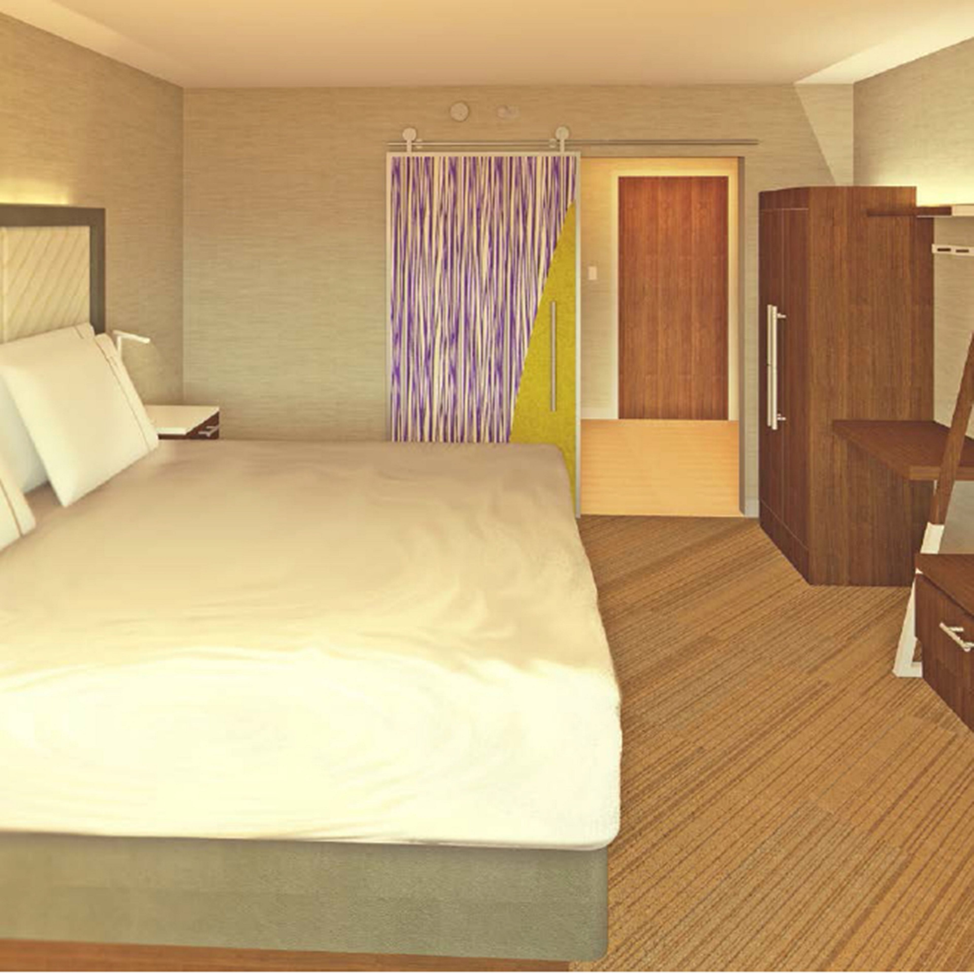 A hotel room with a large bed, a wooden wardrobe, a desk, and a bathroom with a shower curtain.