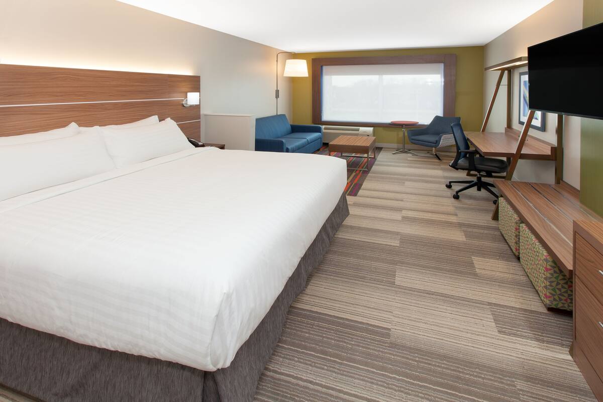 A hotel room with a large bed, a desk with a chair, a sofa, and a TV.