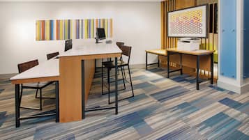 A conference room with a white table, black chairs, a printer, and a colorful abstract painting on the wall.