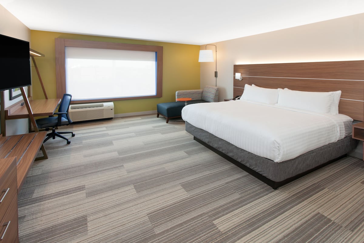 A hotel room with a large bed, a desk with a chair, a TV, and a window with blinds.