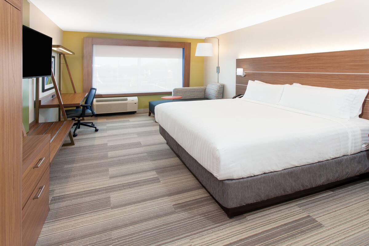 A hotel room with a large bed, a desk with a chair, a TV, and a window with blinds.