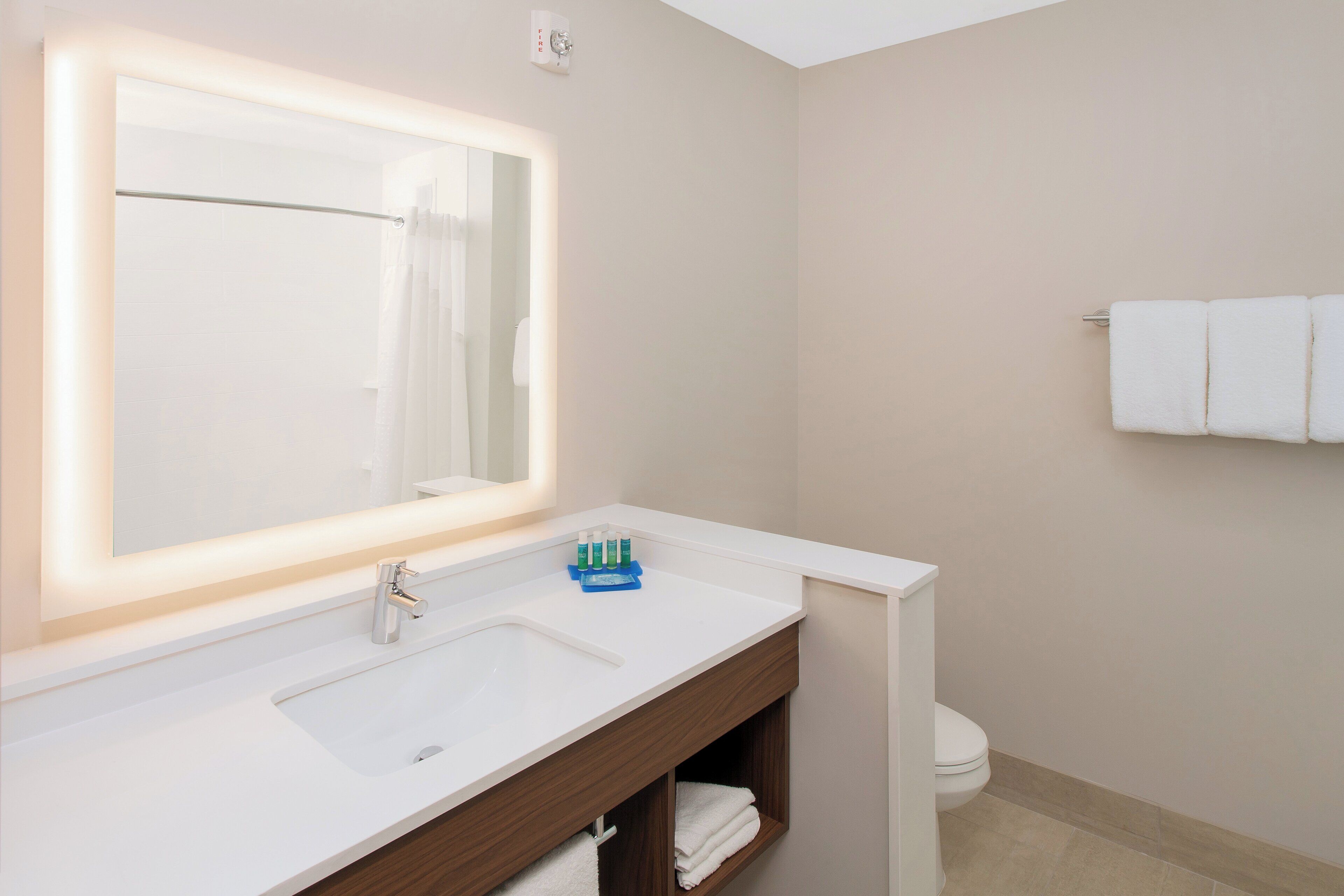 A bathroom with a white sink, a mirror with a light, a toilet, and a towel rack.