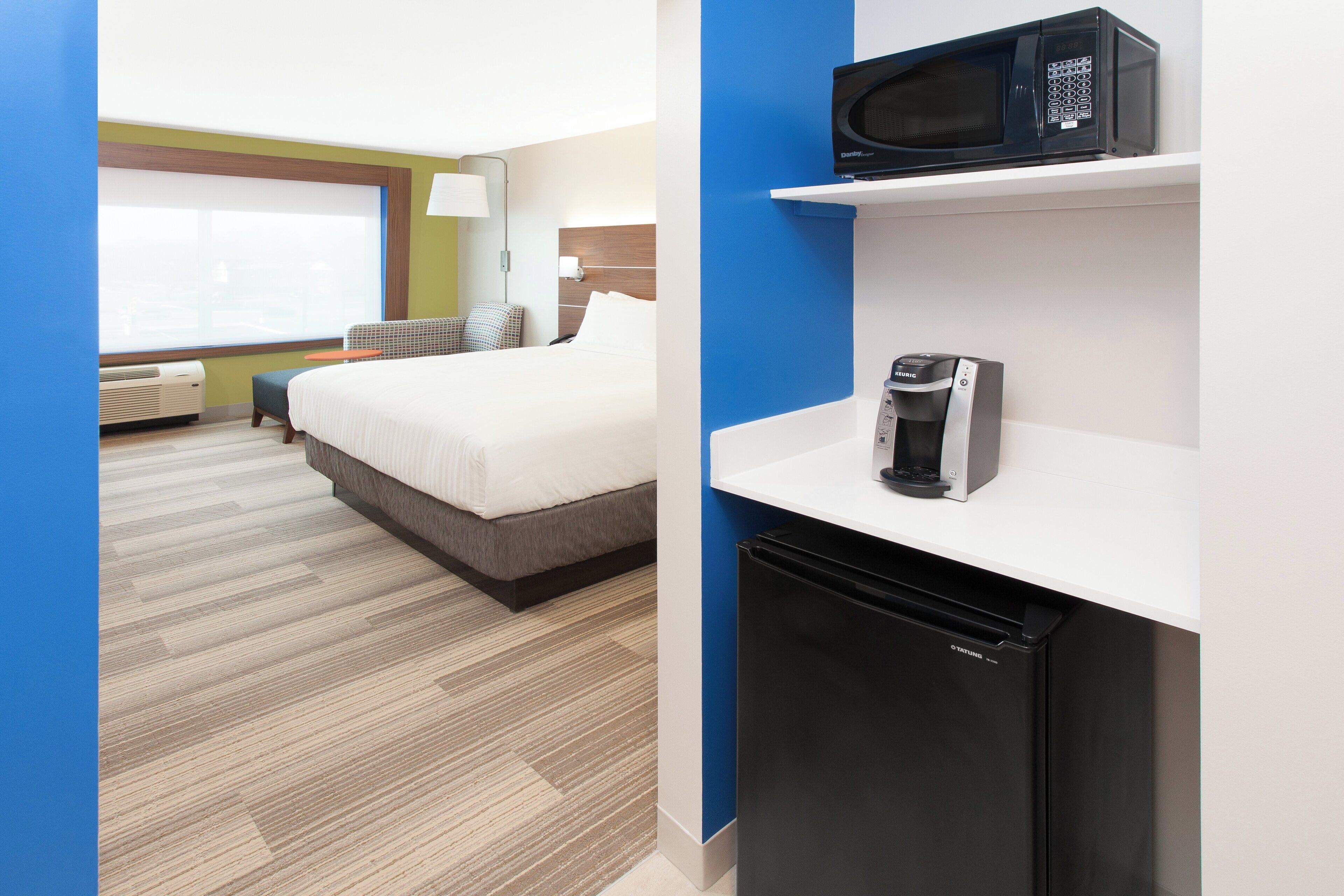 Quarto de hotel com cama, micro-ondas, cafeteira e pequeno frigorífico.