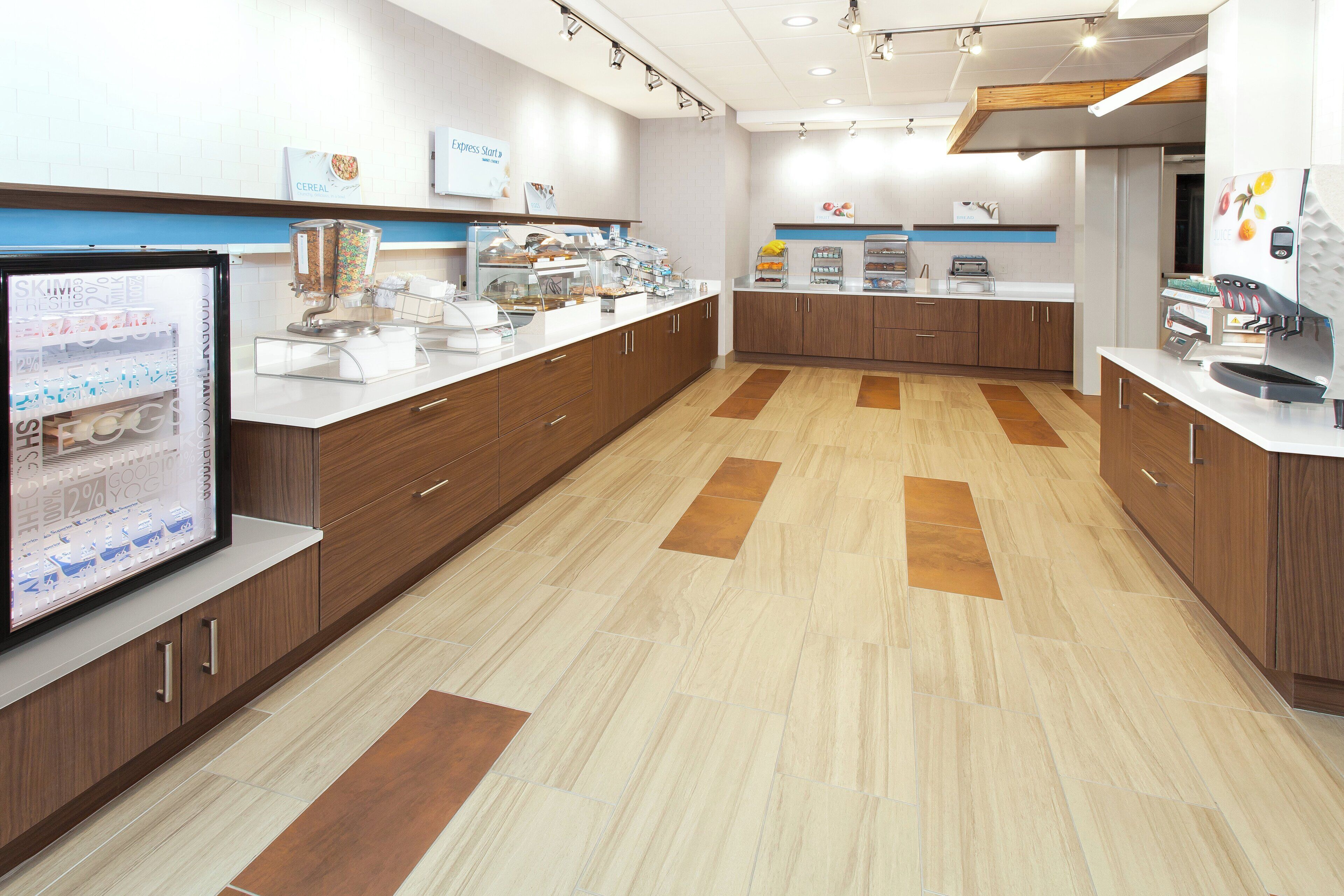 A modern breakfast area with a self-serve station, a coffee machine, and a refrigerator with fruit images.