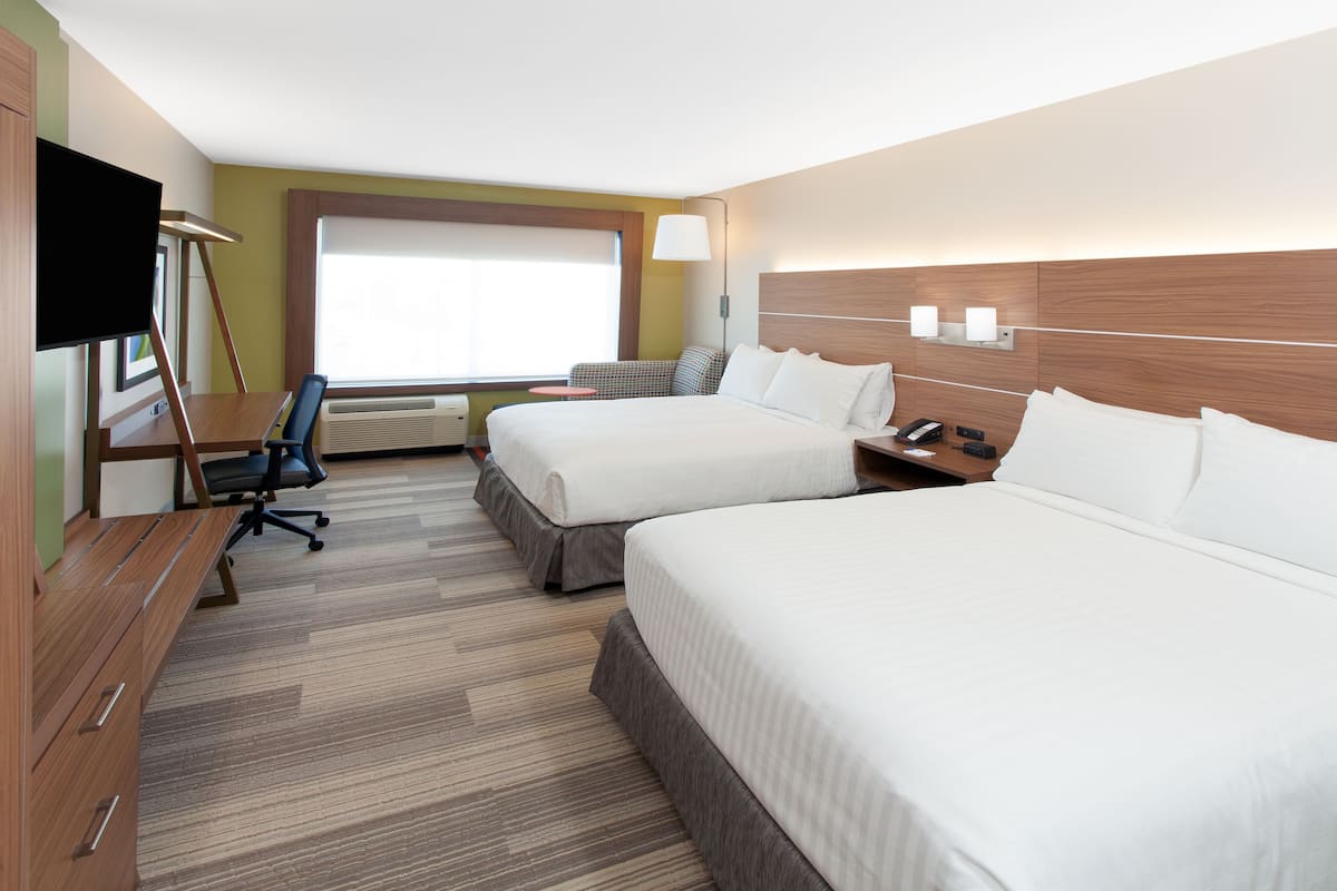 A hotel room with two beds, a desk, a chair, a TV, and a window.