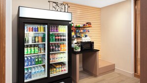 A beverage refrigerator stocked with various drinks, a microwave, and a shelf with snacks and condiments. - Holiday Inn Express and Suites Detroit/Sterling Heights by IHG (Sterling Heights)