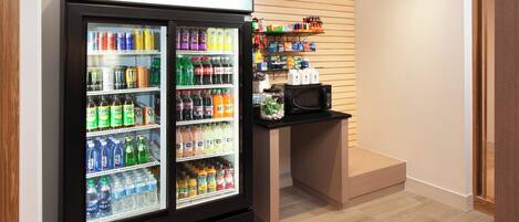 A beverage refrigerator stocked with various drinks, a microwave, and a shelf with snacks and condiments.