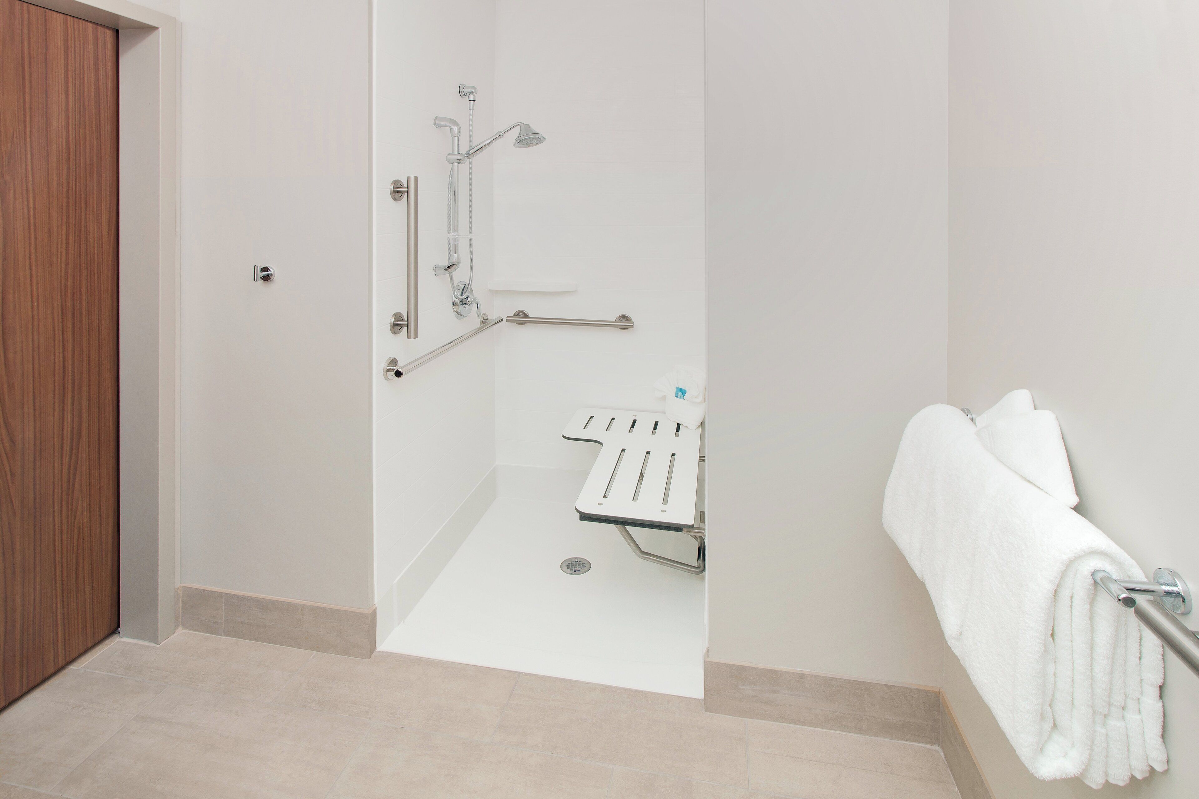 Un baño moderno con cabina de ducha, barras de apoyo, toallero y soporte para papel higiénico.