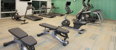 Une salle de sport équipée de tapis de course, de vélos elliptiques et de bancs.