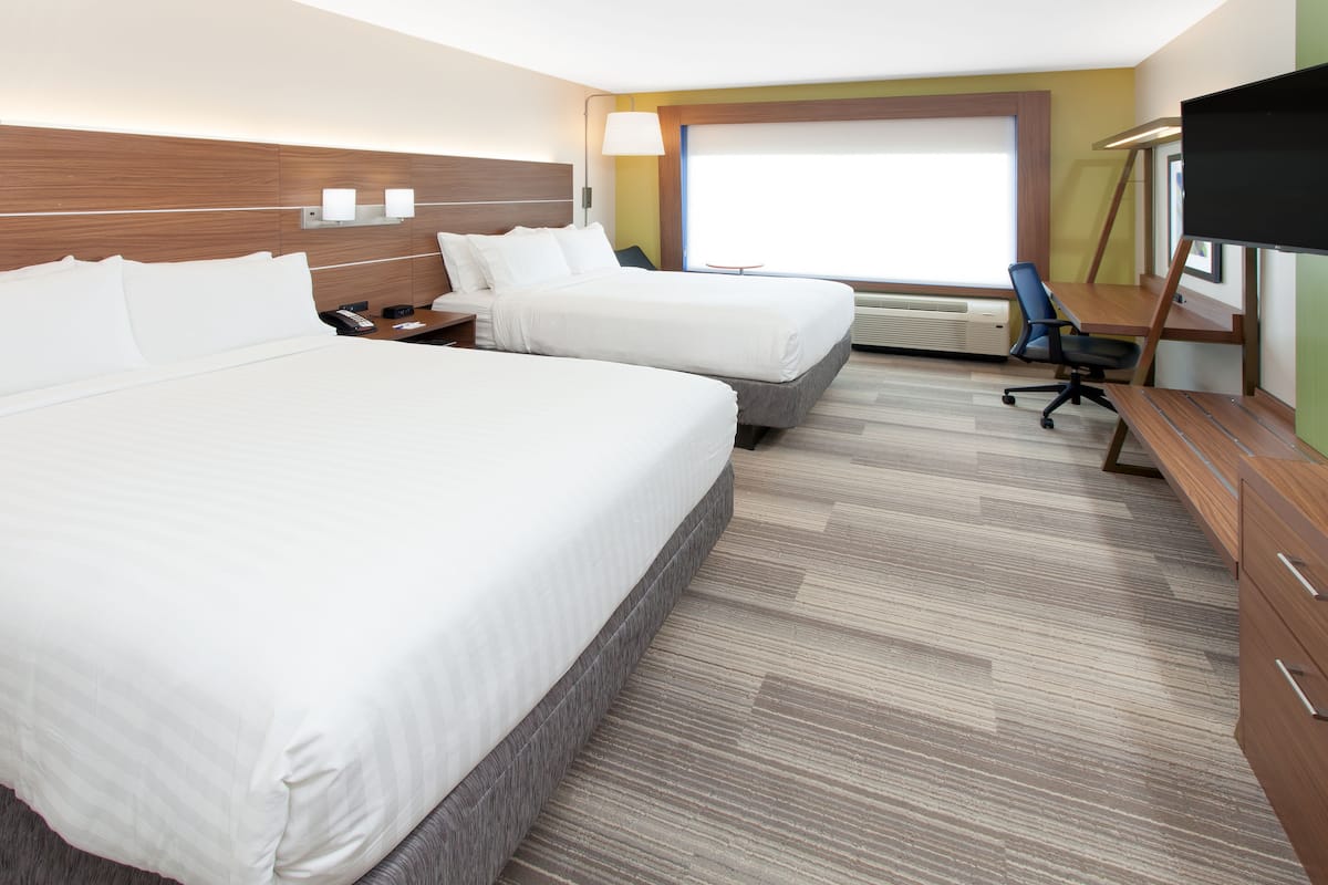 A hotel room with two beds, a desk, a chair, a TV, and a window with blinds.