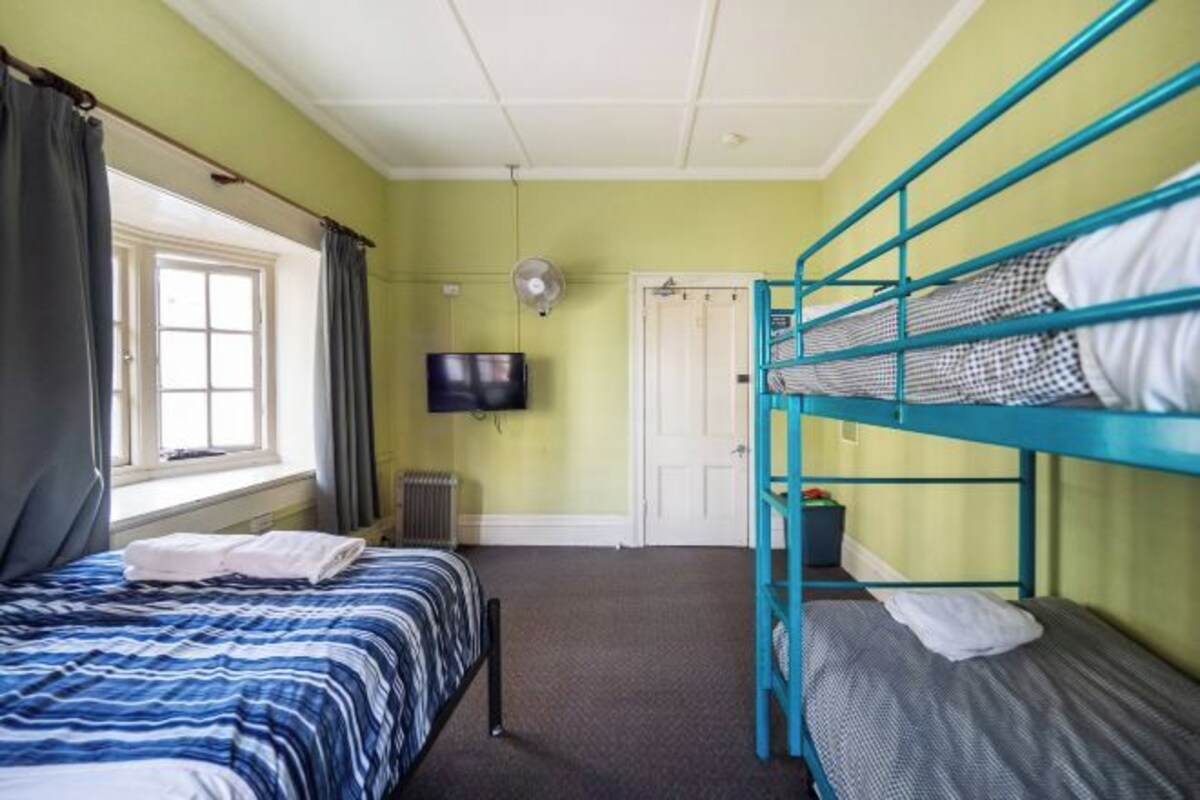 A room with a bunk bed, a single bed, a TV, and a window with curtains.