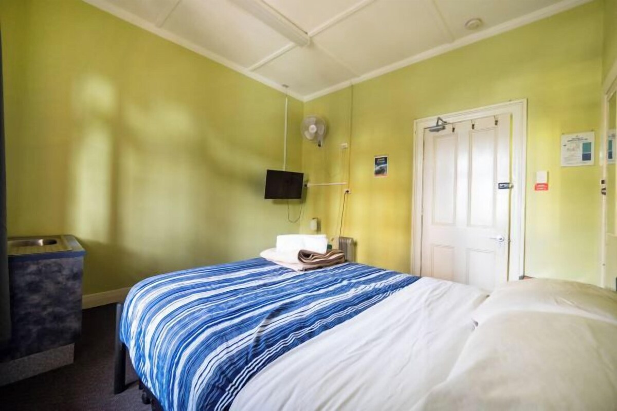 A hotel room with a bed, a television, a door, and a trash bin.