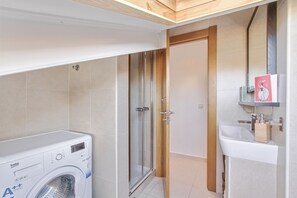 Une petite salle de bain équipée d’un lave-linge, d’une douche à parois de verre et d’un lavabo avec un miroir au-dessus.
