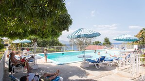 Zona de piscina con sillas de descanso y sombrillas, rodeada por una cerca blanca.