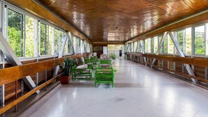 Un paseo techado con bancos y plantas en macetas, grandes ventanales a ambos lados y techo de madera.
