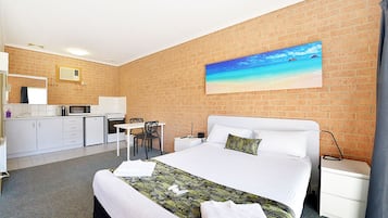 Een hotelkamer met een bed, een bureau, een magnetron, een wastafel en een schilderij van een strand.