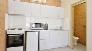A compact kitchen with white cabinets, a microwave, a stove, and a refrigerator. - Cranbourne Motor Inn (Cranbourne)