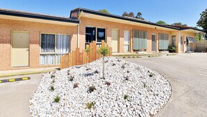 A motel with a brick facade, multiple windows, and a gravel driveway. - Cranbourne Motor Inn (Cranbourne)