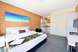 A hotel room with a bed, a desk, a chair, a TV, and a kitchen area.