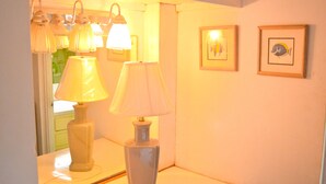 Een kamer met een witte tafel, twee lampen en twee foto's in lijsten aan de muur.