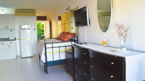 Een slaapkamer met een bed, een dressoir, een televisie, een spiegel en een klein tafeltje met een vaas.