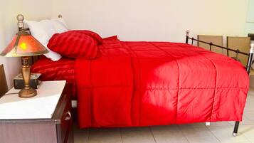 Una cama bien hecha con una colcha y almohadas rojas, una lámpara de noche y una mesita con una lámpara.