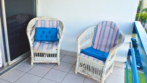 Twee rieten stoelen met gestreepte kussens op een betegeld terras.