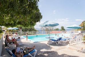 A pool area with lounge chairs and umbrellas, surrounded by a white fence.
