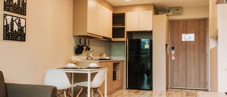 A compact kitchen with a dining area, a refrigerator, and a wooden door.