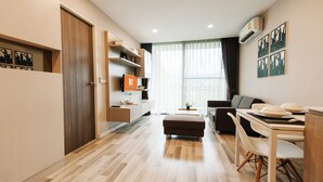 A modern living room with a sofa, a dining table with chairs, a wooden floor, and a large window with curtains. - B2 Mountain Pano Residence Chiang Mai (Chiang Mai)