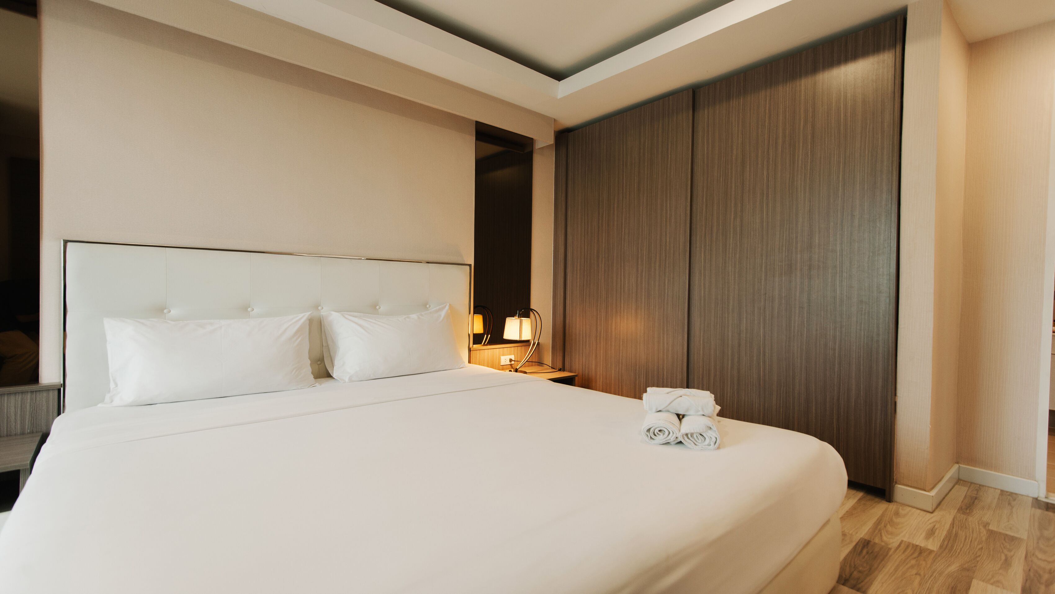 A hotel room with a large bed, a bedside table with a lamp, and a wooden wardrobe.