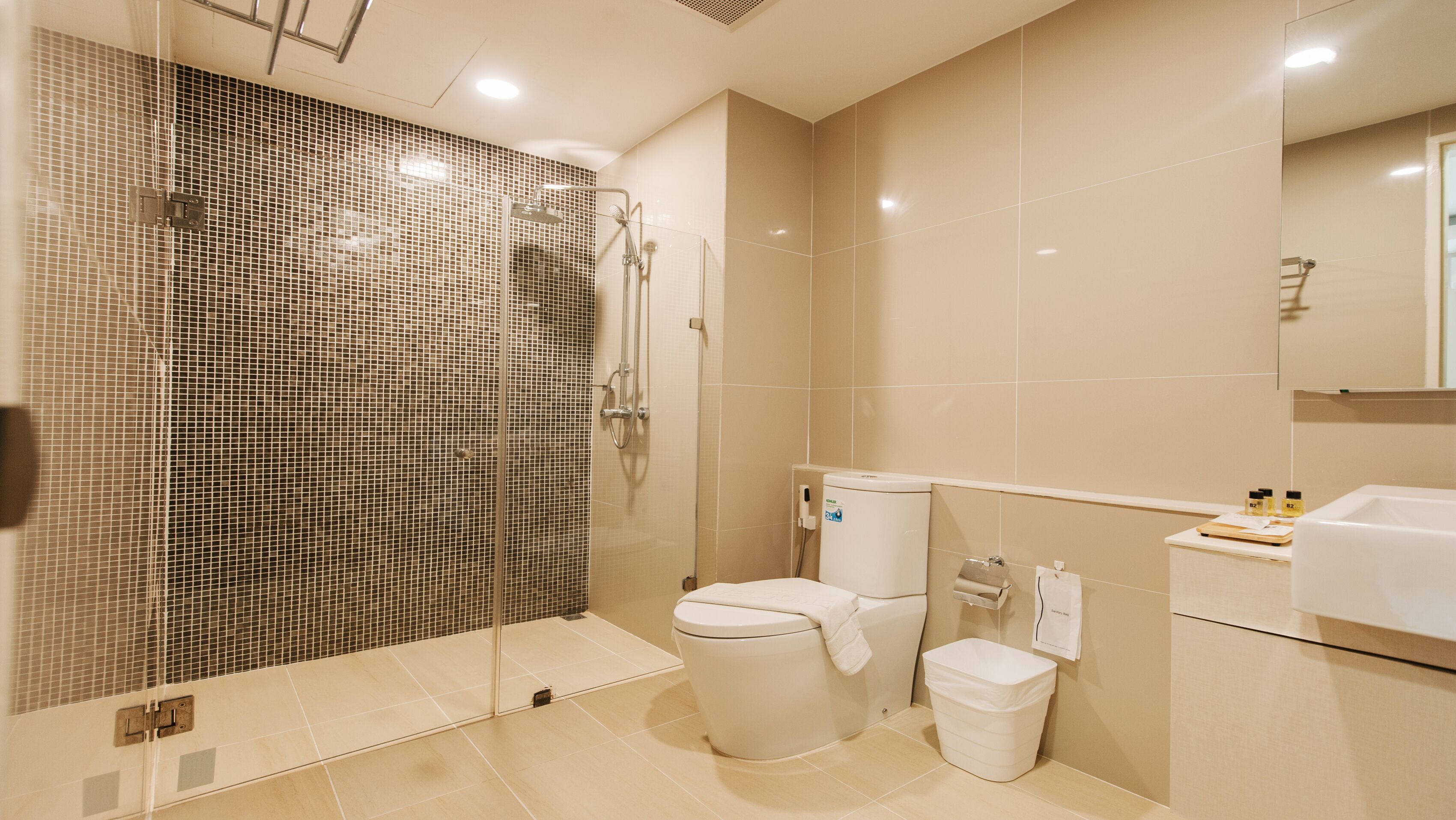 Un baño moderno con ducha de vidrio, inodoro, bidé y lavamanos con artículos de aseo.